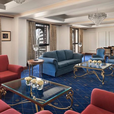 Intercontinental Dar Al Iman Madinah By Ihg Hotel Medina Kültér fotó The photo shows a luxurious living space or lounge area. It features a combination of furniture, including a blue sofa, several red armchairs, and glass-top coffee tables with gold accents. The flooring is carpeted in a deep blue, and the walls are a