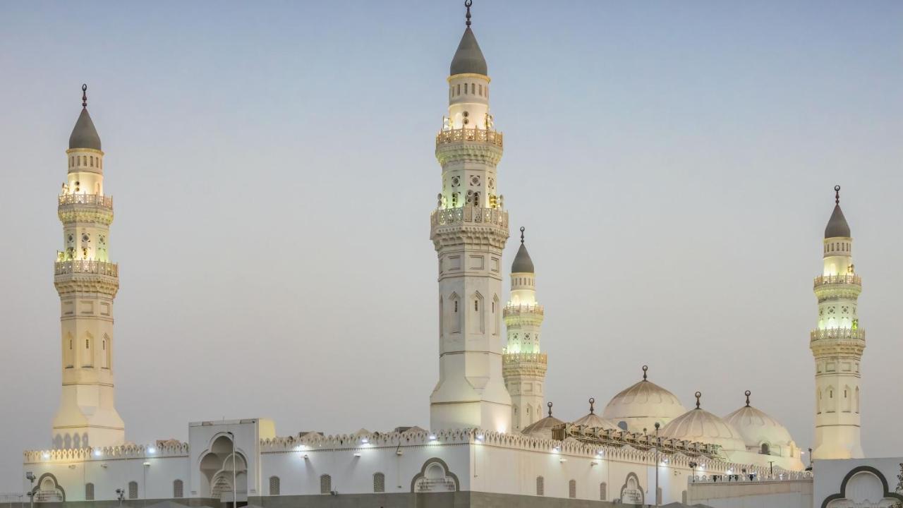 Intercontinental Dar Al Iman Madinah By Ihg Hotel Medina Kültér fotó The image shows a mosque with distinct architectural features, including tall minarets and domes. The minarets are highlighted, likely lit up in the evening, showcasing intricate design elements typical of Islamic architecture. The overall scene conv