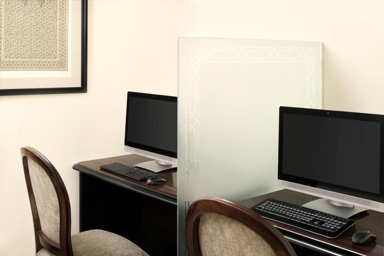 Intercontinental Dar Al Iman Madinah By Ihg Hotel Medina Kültér fotó The photo shows a workspace featuring two computers set up on a dark wooden desk. Each computer has a monitor and a keyboard. A frosted glass partition is placed between the two workstations, providing some privacy. In the background, there is a fram