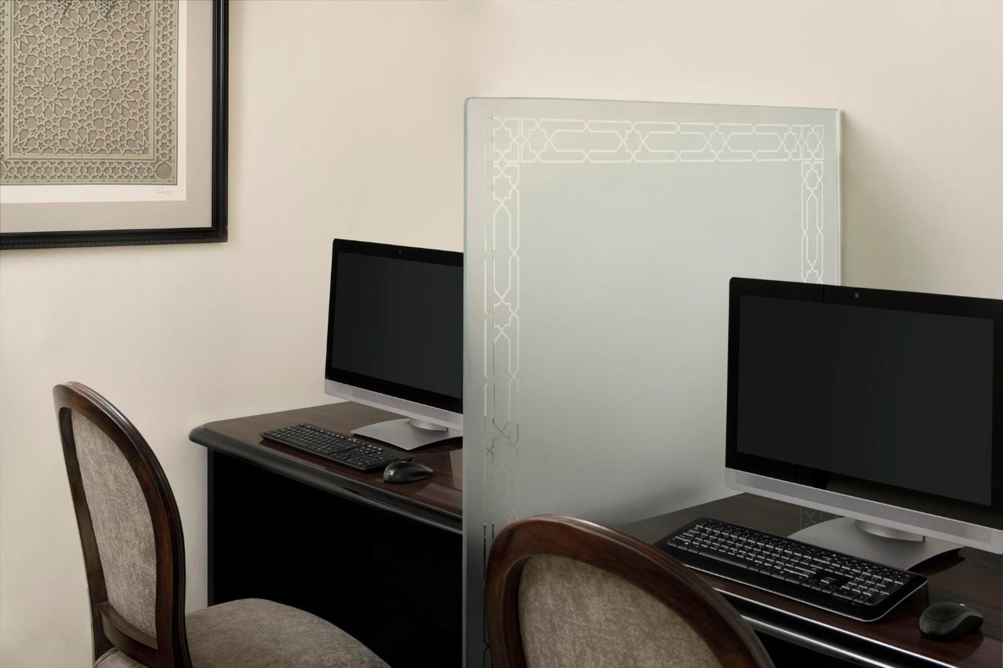 Intercontinental Dar Al Iman Madinah By Ihg Hotel Medina Kültér fotó The photo shows a small office or workspace area featuring two computer stations. Each station has a black monitor, a keyboard, and appears to be set up on a dark wooden desk. A translucent glass partition is placed between the two workstations, prov