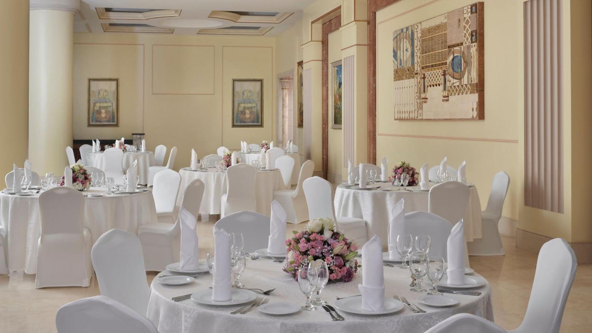 Intercontinental Dar Al Iman Madinah By Ihg Hotel Medina Kültér fotó The photo shows an elegantly arranged dining area, likely set up for a formal event or reception. There are several round tables covered with white tablecloths, each adorned with floral centerpieces featuring pink flowers. The tables are set with pla
