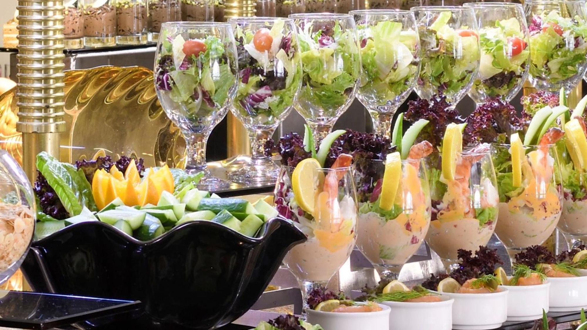 Intercontinental Dar Al Iman Madinah By Ihg Hotel Medina Kültér fotó The photo features an elegant display of food items. In the background, there are several clear glasses filled with vibrant salads, featuring various types of greens and garnishes. In the foreground, there is a decorative black bowl containing cut pi