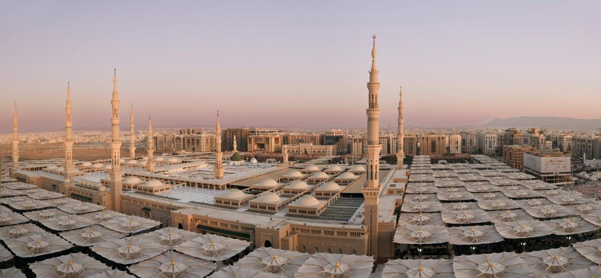 Intercontinental Dar Al Iman Madinah By Ihg Hotel Medina Kültér fotó The photo shows an aerial view of the Al-Masjid an-Nabawi, or the Prophet's Mosque, located in Medina, Saudi Arabia. The mosque features distinct minarets, large white domes, and expansive open areas with large umbrellas that provide shade for visito