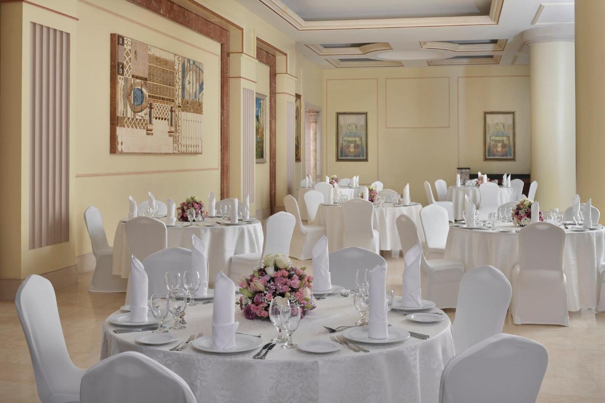 Intercontinental Dar Al Iman Madinah By Ihg Hotel Medina Kültér fotó The photo shows an elegantly arranged dining or function room. There are round tables covered with white tablecloths, each set with fine dining ware including glassware, utensils, and neatly folded white napkins. Some tables have floral centerpieces 