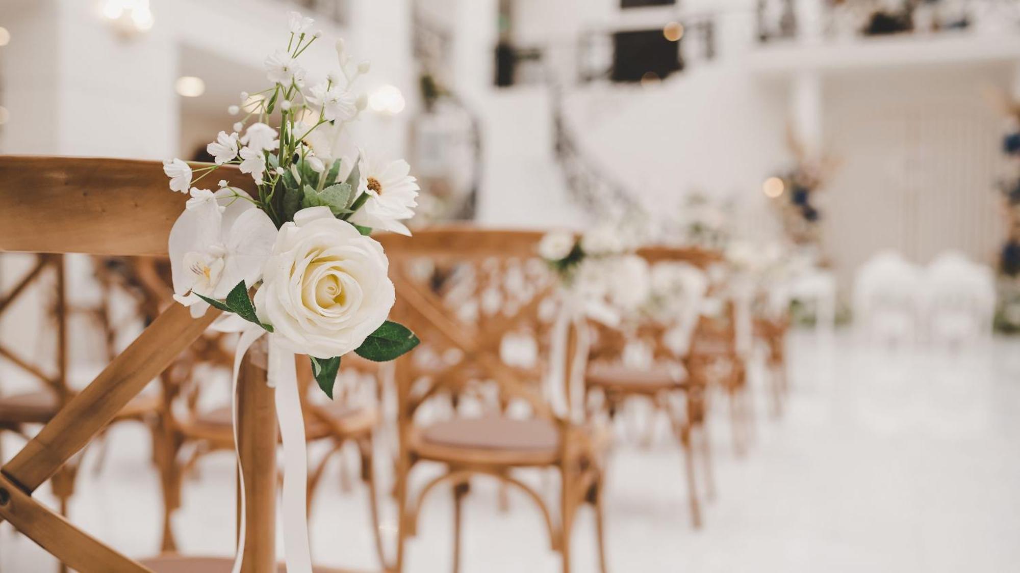 Intercontinental Dar Al Iman Madinah By Ihg Hotel Medina Kültér fotó The photo showcases a beautifully arranged event space, likely set up for a wedding or special occasion. In the foreground, wooden chairs are neatly lined up, some adorned with decorative floral arrangements. The flowers include white roses and small