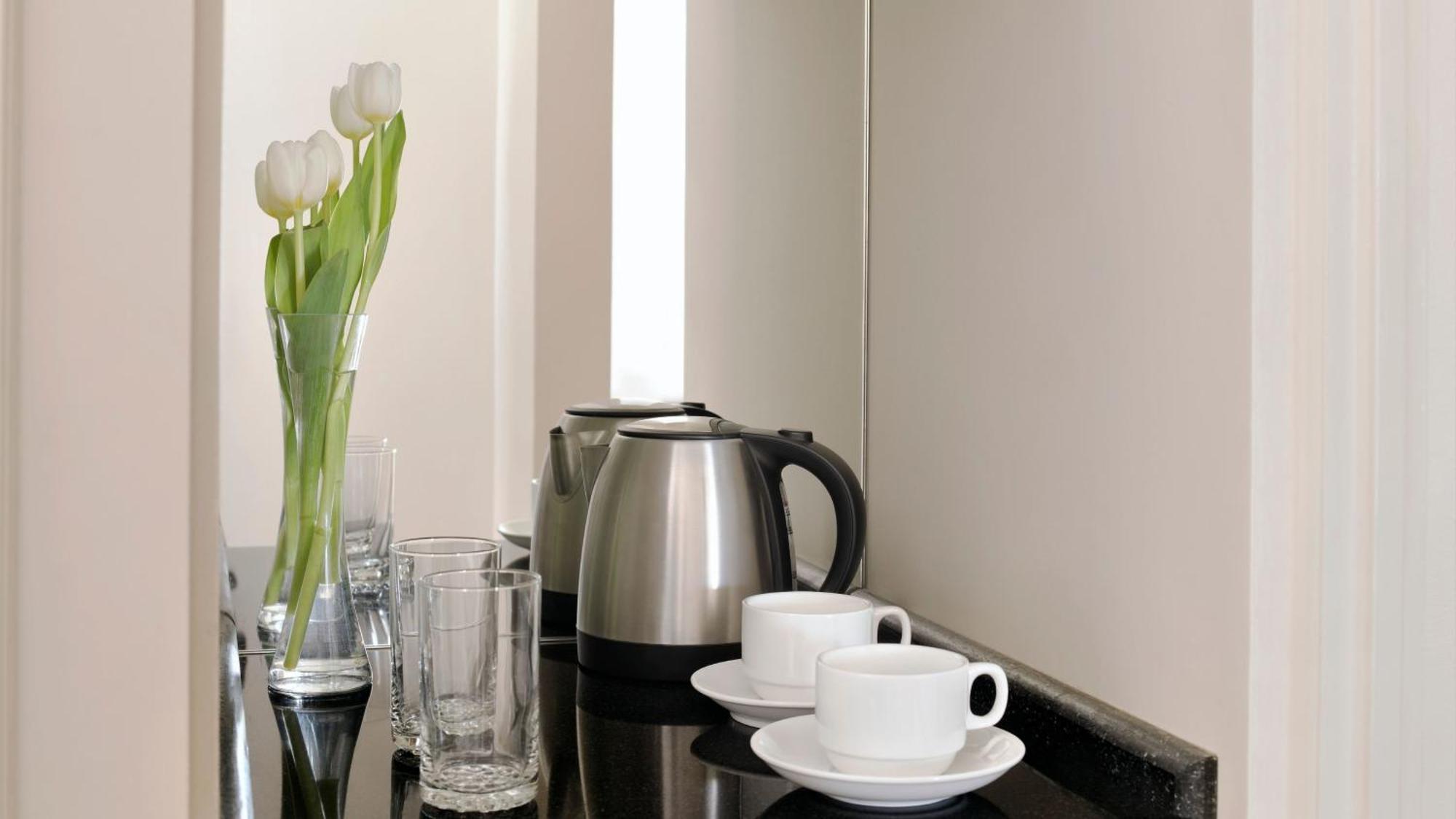 Intercontinental Dar Al Iman Madinah By Ihg Hotel Medina Kültér fotó The photo depicts a neatly arranged beverage area. In the foreground, there are two white coffee cups on small saucers. Next to them, there are two clear drinking glasses. In the background, there is a silver electric kettle, which is positioned next