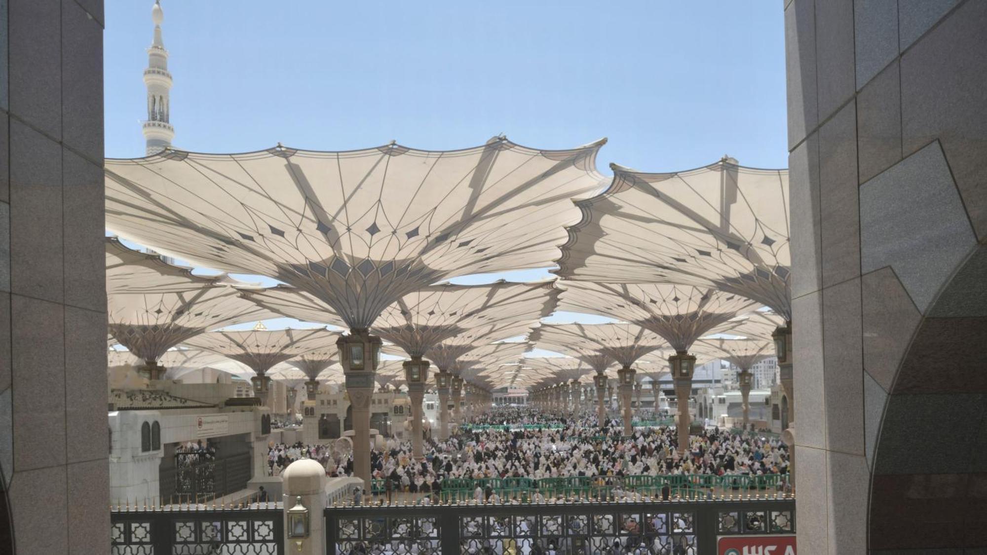 Intercontinental Dar Al Iman Madinah By Ihg Hotel Medina Kültér fotó The photo shows a large open area covered by expansive canopies, likely designed to provide shade for the people below. Underneath the canopies, there are many individuals gathered, possibly participating in a religious event or gathering. In the bac
