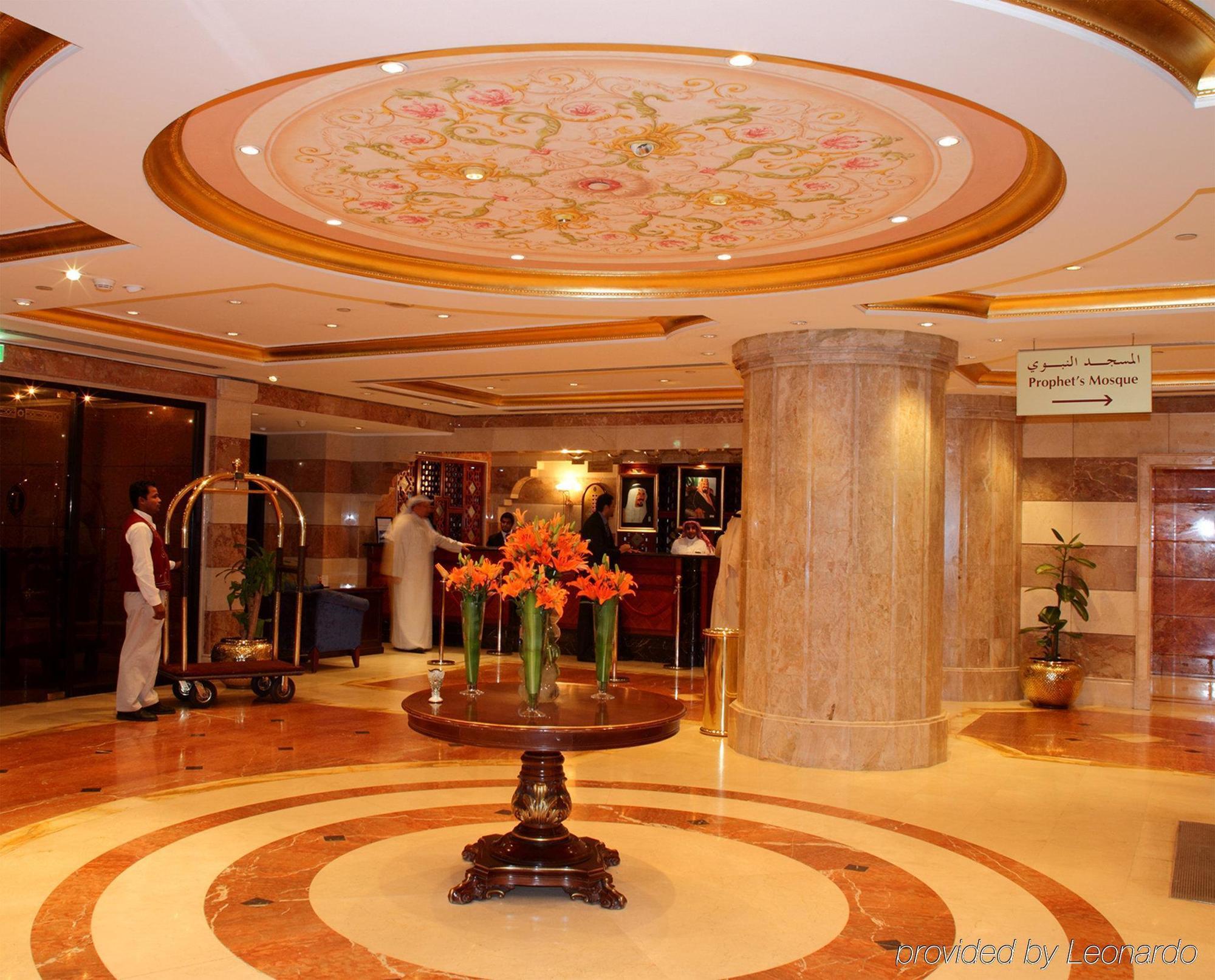 Intercontinental Dar Al Iman Madinah By Ihg Hotel Medina Beltér fotó The photo depicts a luxurious hotel lobby. The ceiling features an ornate design with floral patterns, adding elegance to the space. In the center of the lobby, there is a decorative table with a bowl or vase of bright orange flowers. The flooring is