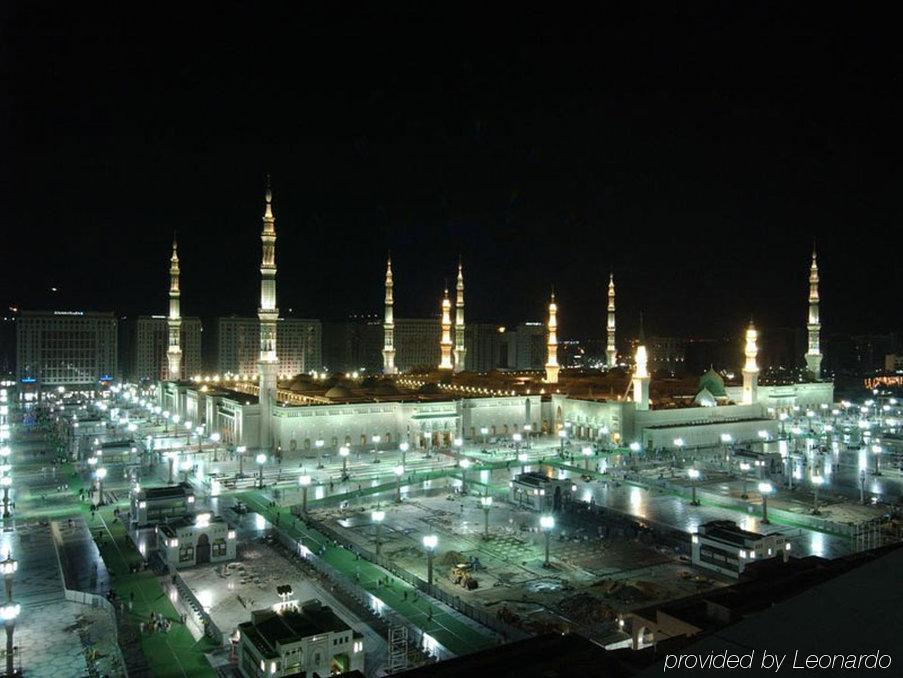 Intercontinental Dar Al Iman Madinah By Ihg Hotel Medina Felszereltség fotó The image shows the illuminated landscape of a mosque complex at night. It features several tall minarets, which are typically part of Islamic architecture, adorned with lights. The mosque's central building is also brightly lit, surrounded by an ope