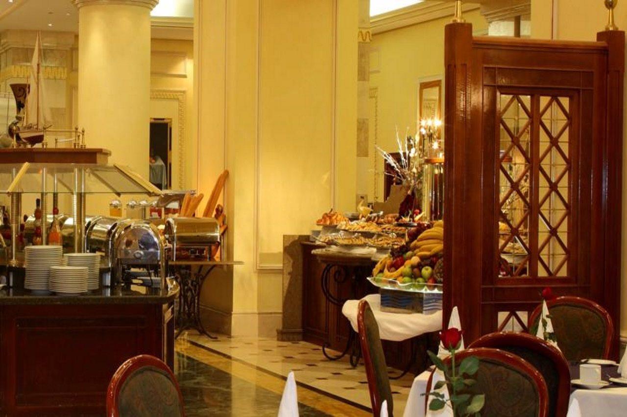 Intercontinental Dar Al Iman Madinah By Ihg Hotel Medina Kültér fotó The photo shows an elegant dining area, likely within a restaurant or a hotel. There's a buffet setup on one side with various food items displayed, including pastries and fruits. The room features warm lighting, polished floors, and decorative walls