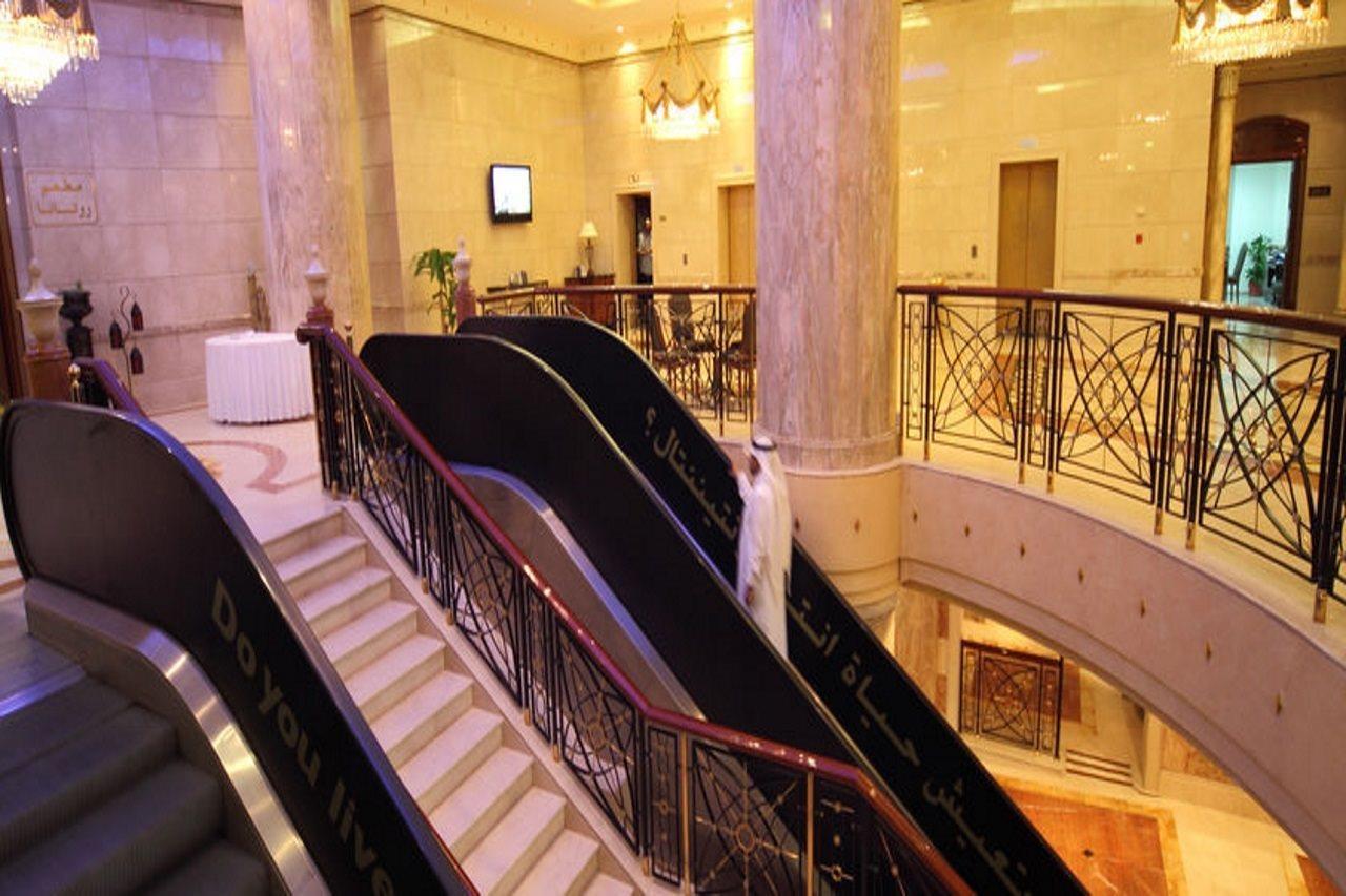 Intercontinental Dar Al Iman Madinah By Ihg Hotel Medina Beltér fotó The photo depicts an elegant interior space, likely within a hotel or a large building. There is a grand staircase visible, which features a combination of stairs and escalators. The design includes decorative railings and marble pillars, contributin