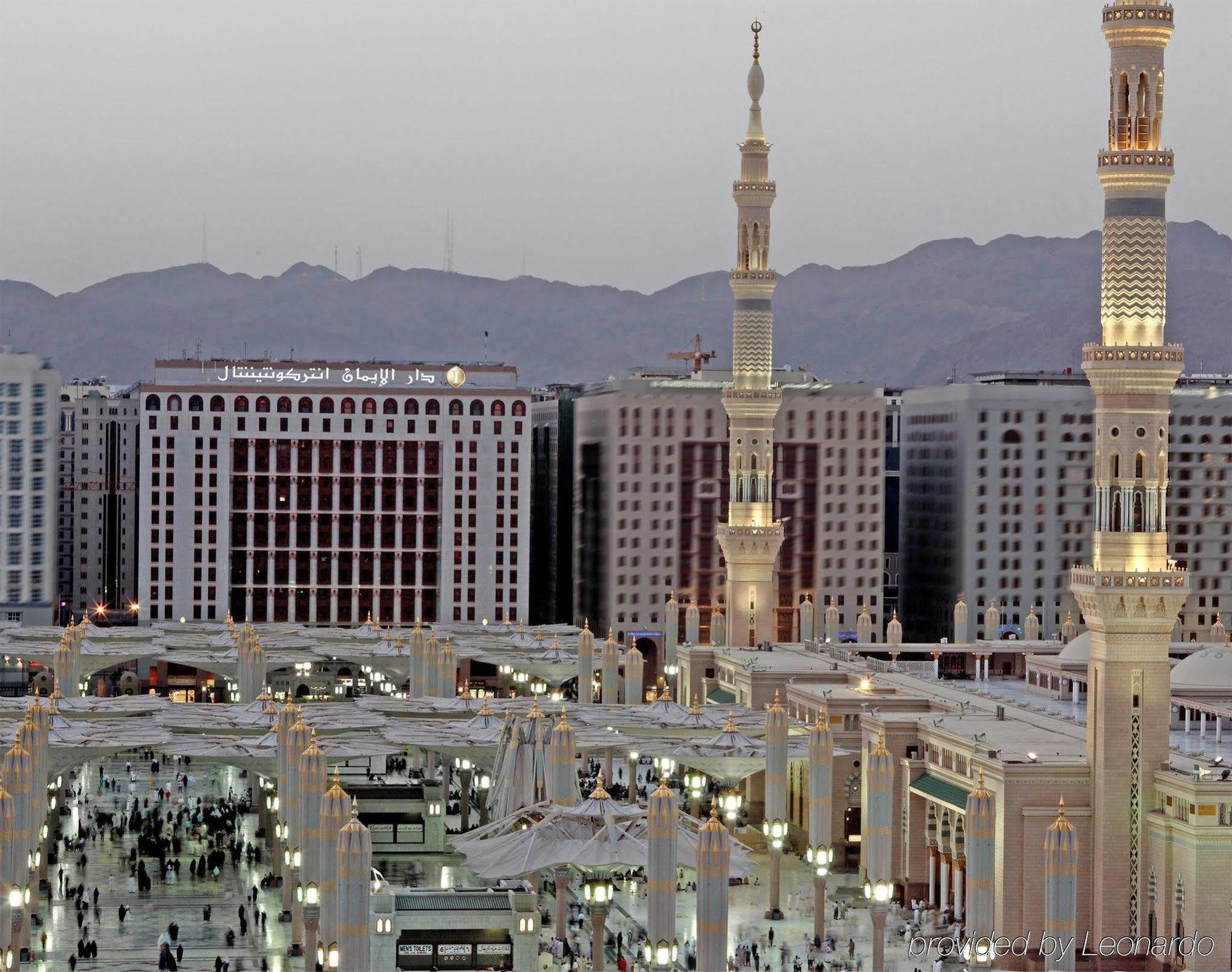 Intercontinental Dar Al Iman Madinah By Ihg Hotel Medina Kültér fotó The photo shows a view of the city of Medina in Saudi Arabia, highlighting the architectural features of the area around a prominent mosque. The structures include tall minarets, which are common in Islamic architecture, and modern buildings in the b